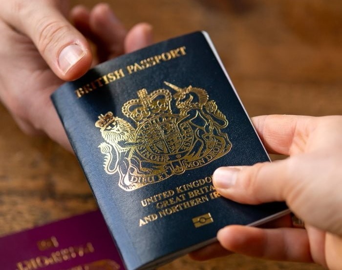 Image of a blue passport being passed over a wood table