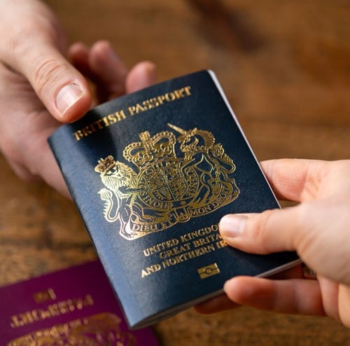 Image of a blue passport being passed over a wood table