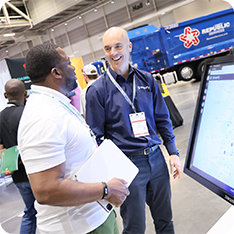 A wastexpo attendee discussing products with an exhibitor in front of a large touchscreen