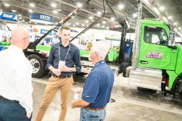 A wastexpo attendee discussing products with an exhibitor in front of a large touchscreen