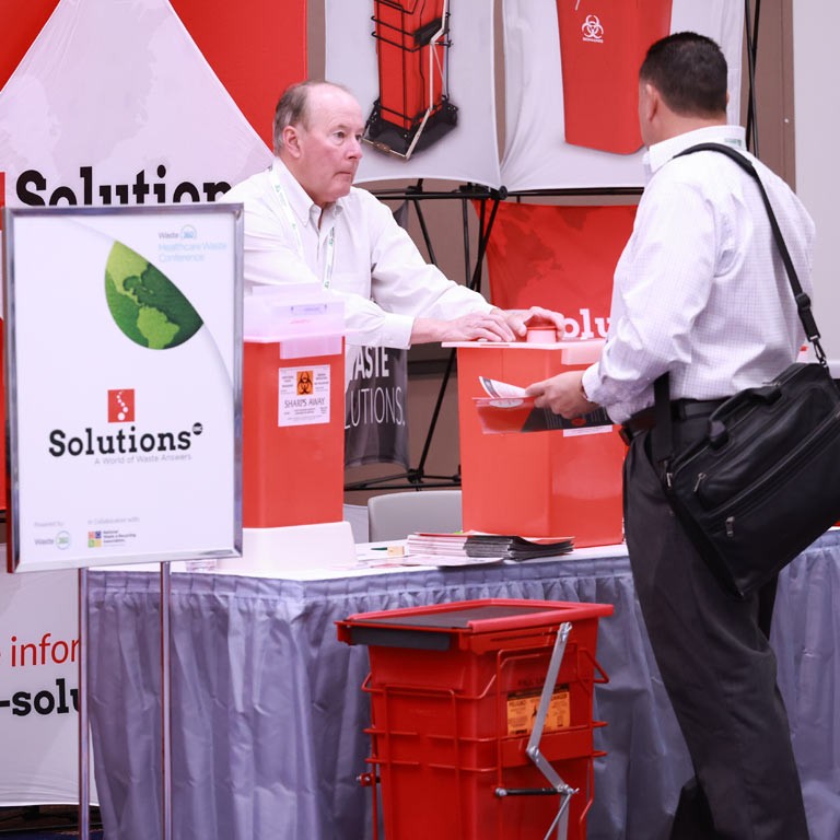 Attendee and Exhibitor shaking hands in front of a Healthcare Waste Conference tabletop