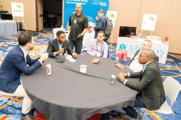 Group of 5 Healthcare Waste conference attendees sitting at a table having a discussion.